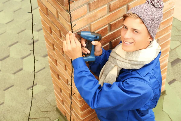 Junger Mann hängt Weihnachtsbeleuchtung an Schornstein des Hauses — Stockfoto