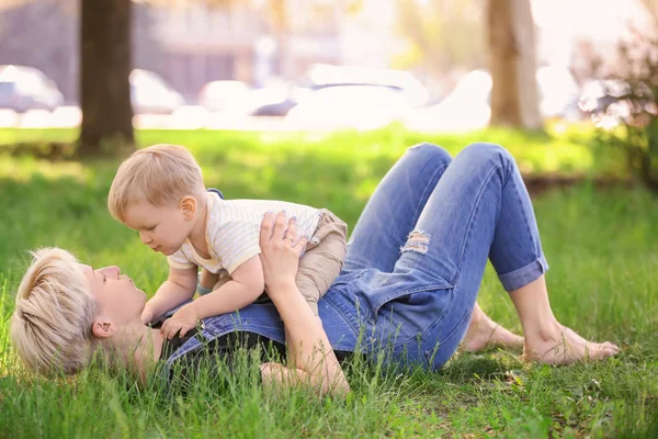 Madre y lindo bebé niño acostado en la hierba verde en el parque — Foto de Stock