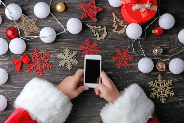 Santa Claus holding phone at wooden table — Stock Photo, Image