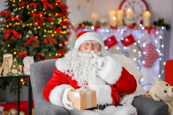 Authentic Santa Claus with gift box sitting in armchair at room decorated for Christmas — Stock Photo, Image