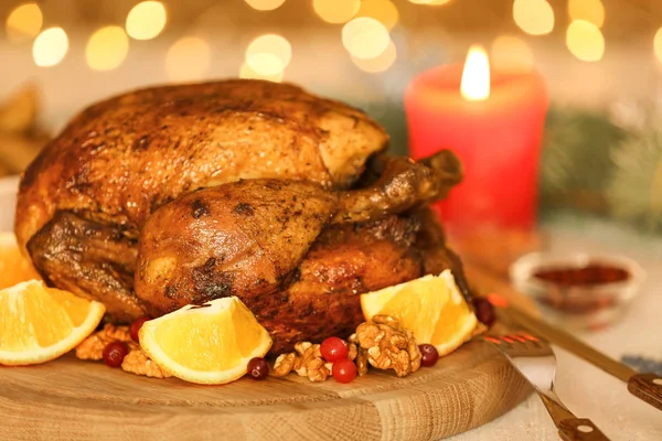 Composition with whole roasted turkey, walnut and oranges on wooden board against defocused lights