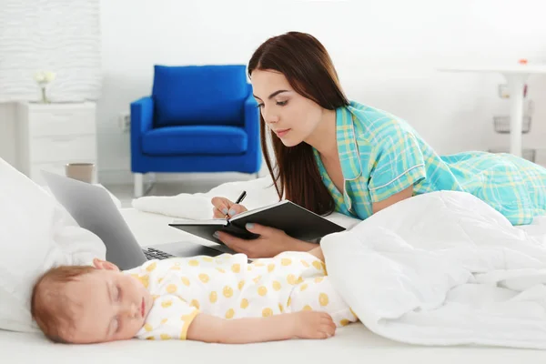 Young mother working near sleeping baby in bedroom — Stock Photo, Image