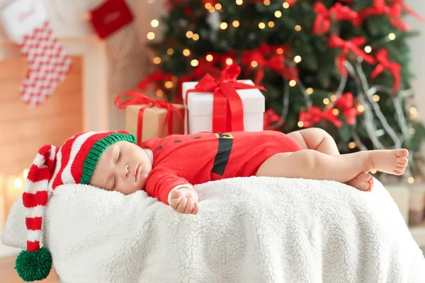Симпатичный малыш в костюме Санты спит на фоне размытых рождественских огней — стоковое фото