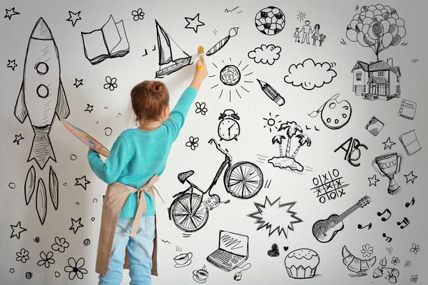 Cute little girl drawing on light wall. Different sketches on background — Stock Photo, Image