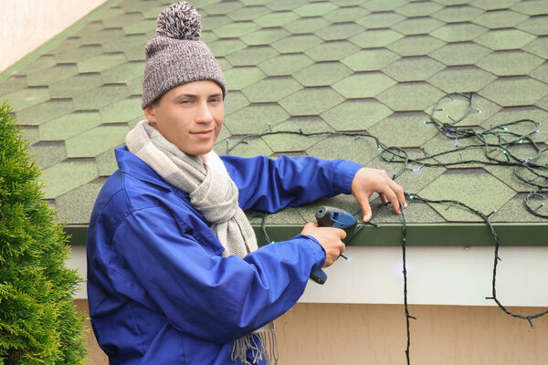 Young man hanging Christmas lights on roof of house