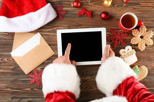 De tablet van de holding van de Kerstman bij houten tafel — Stockfoto