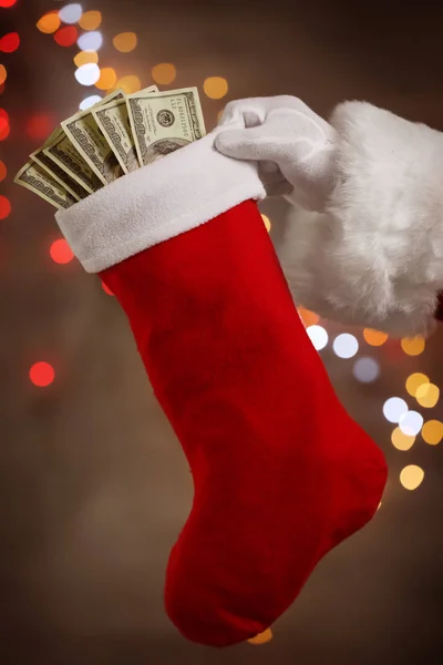 Santa Claus holding stocking with money against defocused lights — Stock Photo, Image