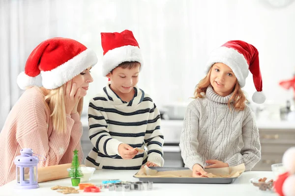 Mujer joven preparando galletas de Navidad con niños pequeños en la cocina — Foto de Stock