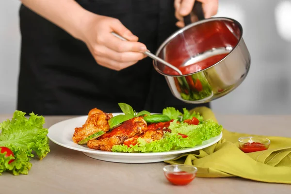 Kobieta, wlewając sos na talerz z danie z kurczaka na stole — Zdjęcie stockowe