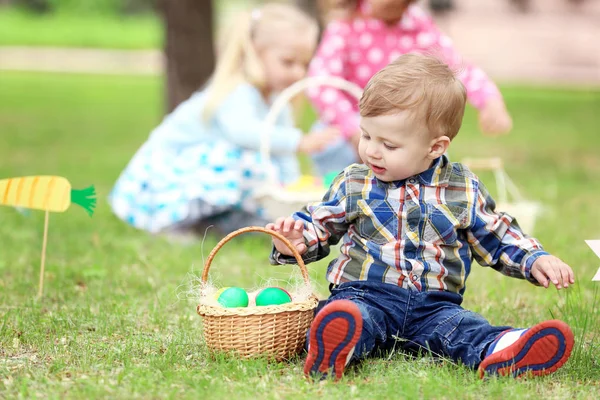 Милый маленький мальчик с корзинкой на зеленой траве в парке. Концепция охоты на пасхальные яйца — стоковое фото