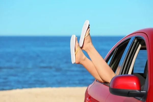Legs of beautiful young woman relaxing in car at sea shore — Stock Photo, Image