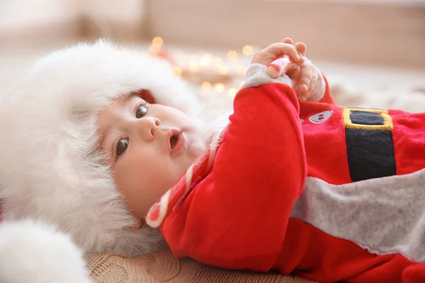 Fröhliches süßes Baby im Weihnachtsmann-Anzug mit Süßigkeiten auf Strickstoff liegend — Stockfoto