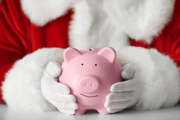 Santa Claus holding piggy bank at table — Stock Photo, Image