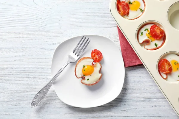 Teller und Muffindose mit leckeren Eiern im Schinken auf dem Tisch — Stockfoto