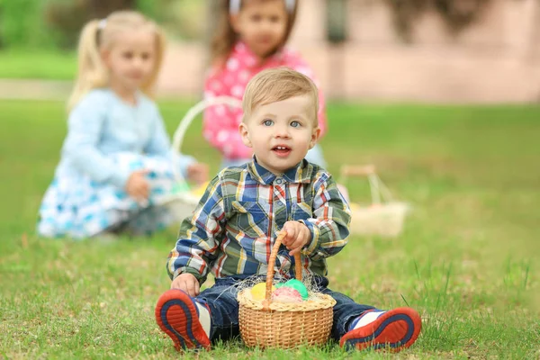Schattige kleine jongen met mandje op groen gras in park. Easter egg hunt concept — Stockfoto