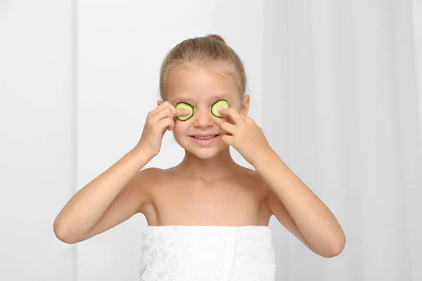 Kleines nettes Mädchen mit Gurkenscheiben auf Augen vor hellem Hintergrund. Schönheitskonzept — Stockfoto