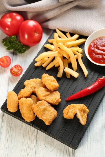 Smakelijke nuggets, frietjes en kommetje met saus voor kip op houten plank — Stockfoto