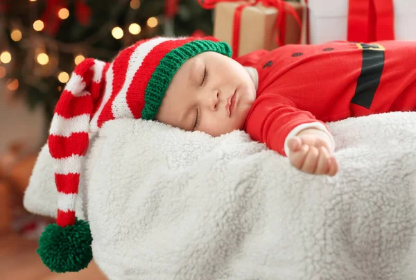 Schattige kleine baby in Santa kostuum slapen tegen Kerstmis lights achtergrond wazig — Stockfoto