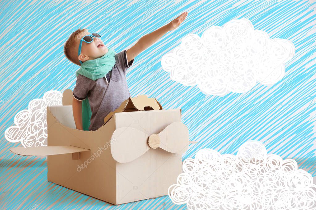 Little boy playing with cardboard airplane and drawing of sky on background
