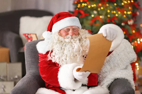 Auténtico Santa Claus con hoja de papel sentado en sillón en la habitación decorada para Navidad —  Fotos de Stock