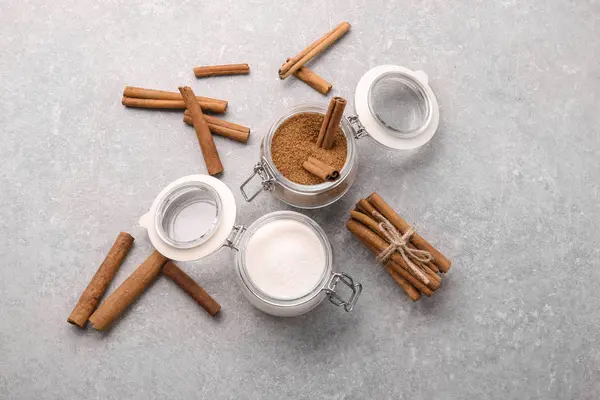 Composition with cinnamon and white sugar in glass jars on grey background — Stock Photo, Image