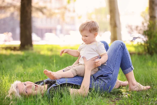 Madre y lindo bebé niño acostado en la hierba verde en el parque — Foto de Stock