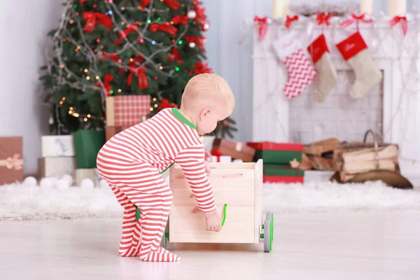 Niedliches kleines Baby spielt mit Spielzeugwagen im weihnachtlich dekorierten Zimmer — Stockfoto