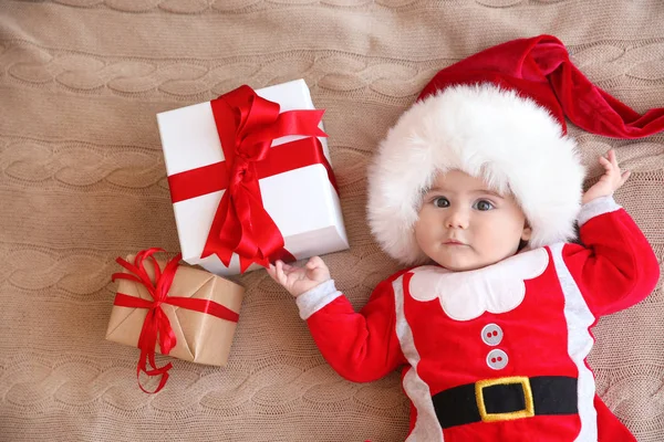 Fröhliches süßes Baby im Weihnachtsmann-Anzug mit Geschenkschachteln auf Strickstoff liegend — Stockfoto