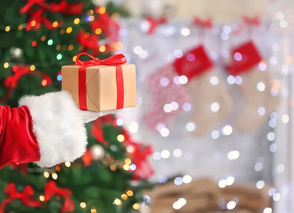 Санта-Клаус держит подарочную коробку против размытых рождественских огней — стоковое фото
