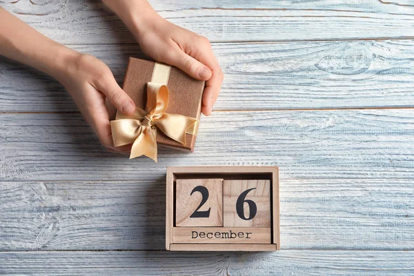 木製の背景にギフト ボックスと日付でカレンダーを保持している女性の手。クリスマス コンセプト — ストック写真