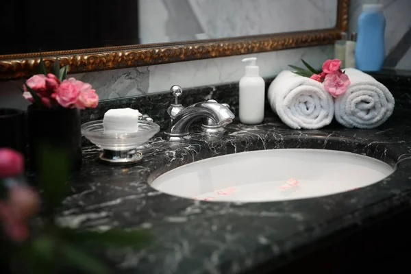 Cosmetics and towels near sink with petals in bathroom. Spa concept — Stock Photo, Image