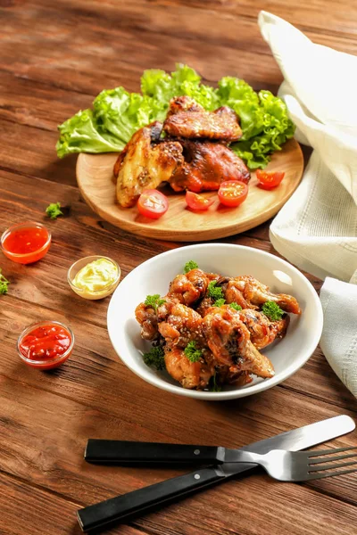 Вкусная курица и маленькие миски с соусами на деревянном столе — стоковое фото
