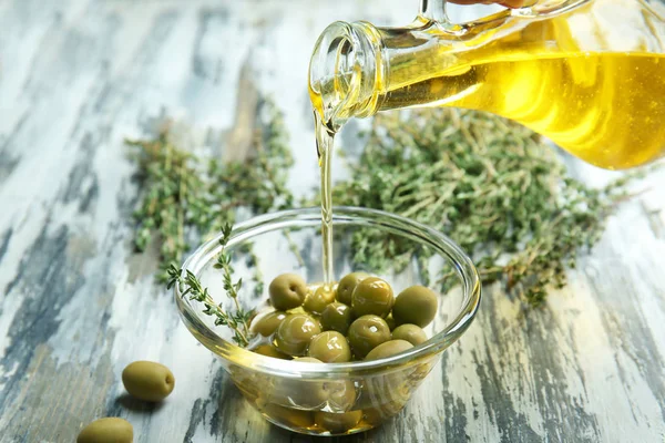 Pouring cooking oil into bowl with olives on wooden table