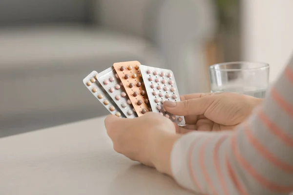 Mujer sosteniendo píldoras anticonceptivas en la mesa — Foto de Stock