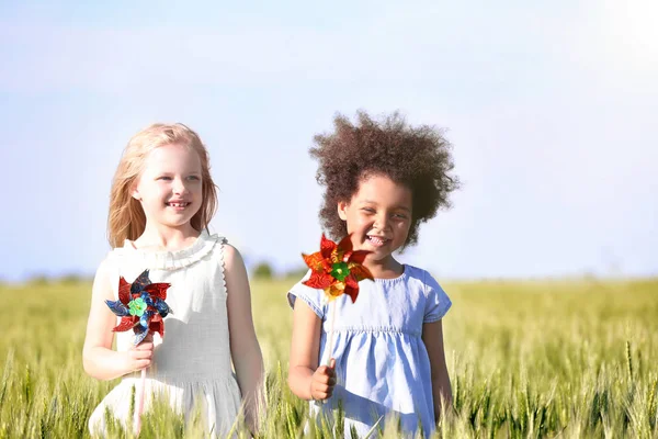 Счастливые маленькие девочки с игрушечными ветряными мельницами в зеленом поле — стоковое фото