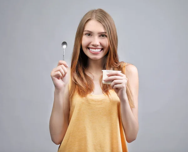 Mujer joven comiendo yogur sobre fondo claro — Foto de Stock