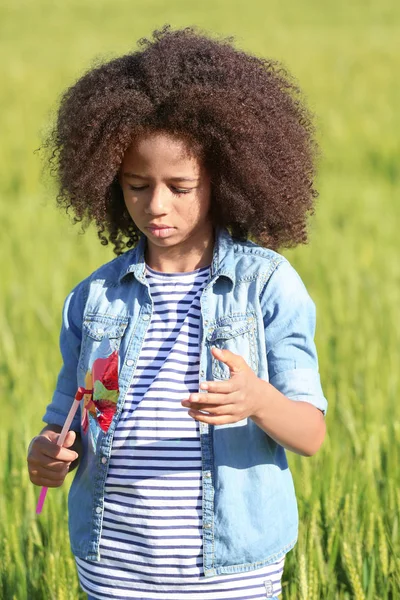 Kleines afroamerikanisches Mädchen mit Spielzeugwindrad im grünen Feld — Stockfoto