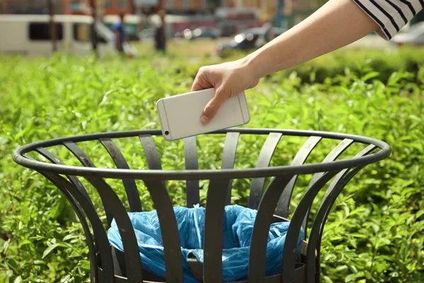 Young woman throwing smartphone in litter bin outdoors