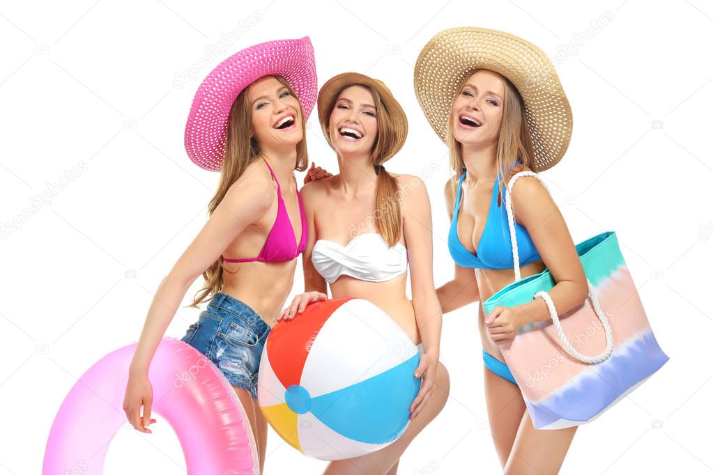 Beautiful young women in bikini with inflatable rubber ring, ball and bag on white background