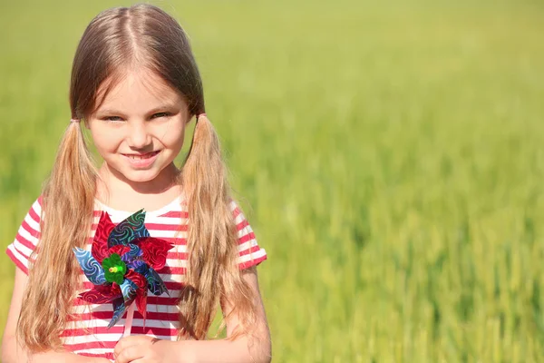 Dziewczynka z zabawka wiatrak w zielone pola — Zdjęcie stockowe