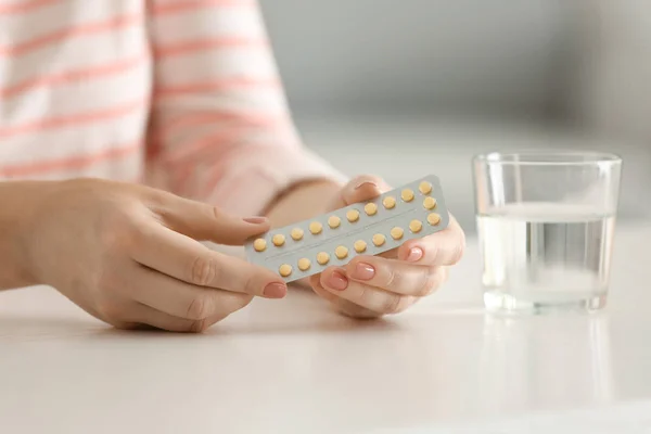 Mujer sosteniendo píldoras anticonceptivas en la mesa — Foto de Stock