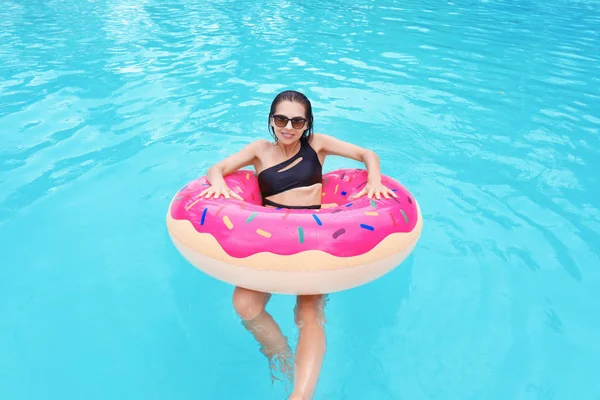 Mulher nova bonita com donut inflável na piscina — Fotografia de Stock