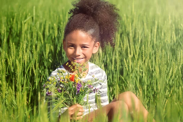 Petite fille afro-américaine avec bouquet de fleurs sauvages dans un champ vert — Photo