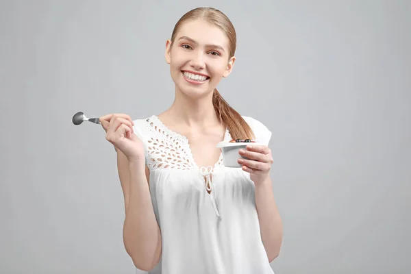 Jonge vrouw yoghurt eten op lichte achtergrond — Stockfoto