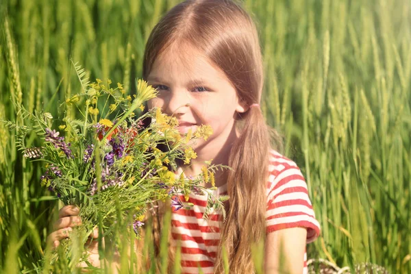 Little girl with bouquet of wildflowers in green field — Stock Photo, Image