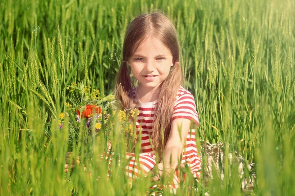 Маленькая девочка с букетом полевых цветов в зеленом поле — стоковое фото