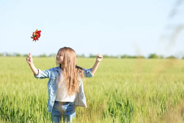 Feliz niña con molino de viento de juguete en el campo verde —  Fotos de Stock