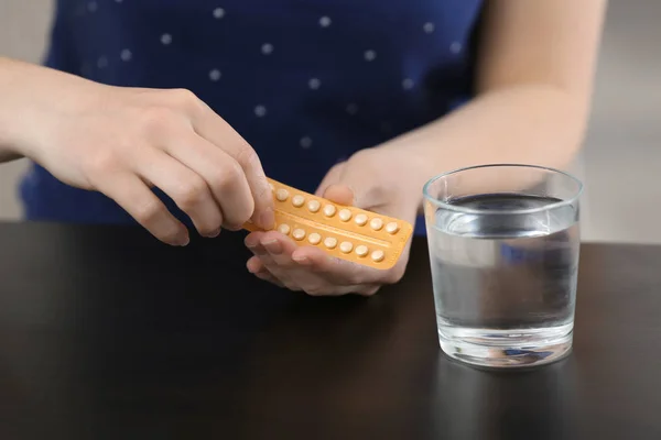 Mujer con píldoras anticonceptivas y vaso de agua en la mesa —  Fotos de Stock