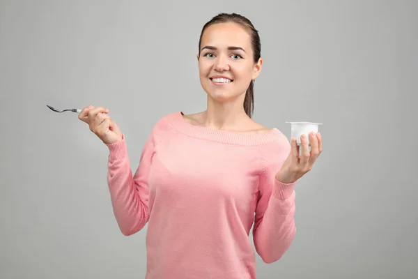 Mujer joven comiendo yogur sobre fondo claro — Foto de Stock