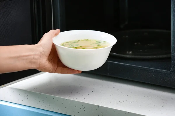 Mulher colocando prato com sopa no forno de microondas. Cozinhar para um conceito — Fotografia de Stock